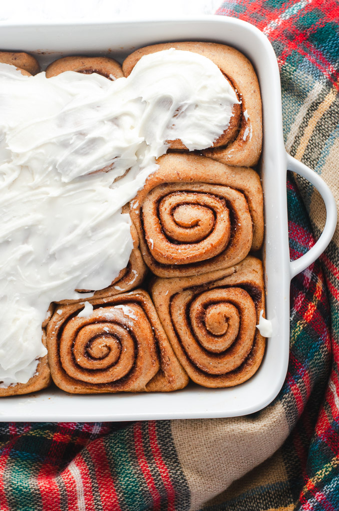 Frosted and unfrosted cinnamon rolls in a white dish on a plaid cloth.