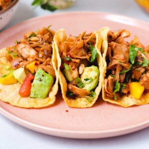 Side view of three corn tortillas filled with jackfruit, avocado and mango