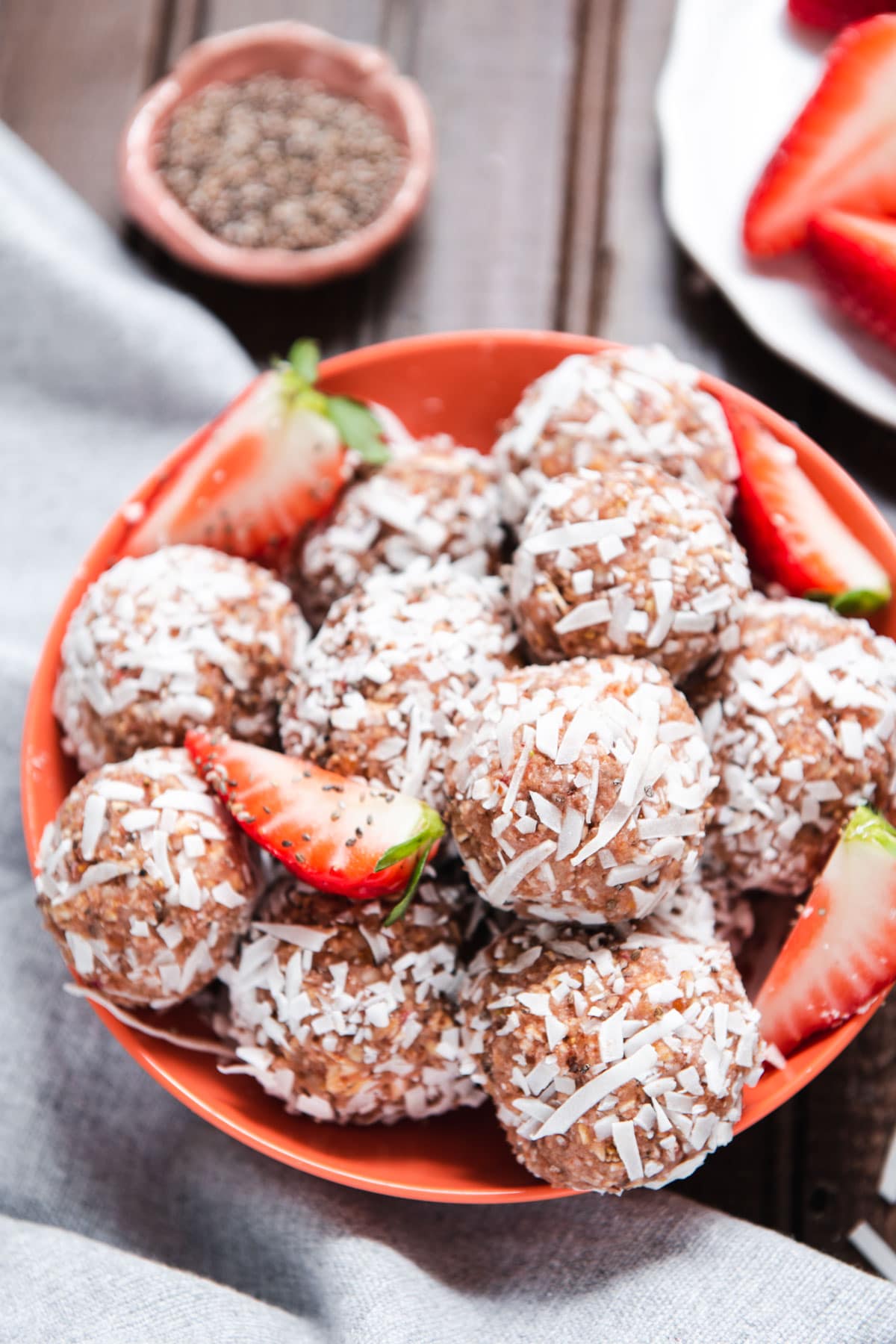 Coconut coated strawberry balls in a pink bowl with strawberry slices.