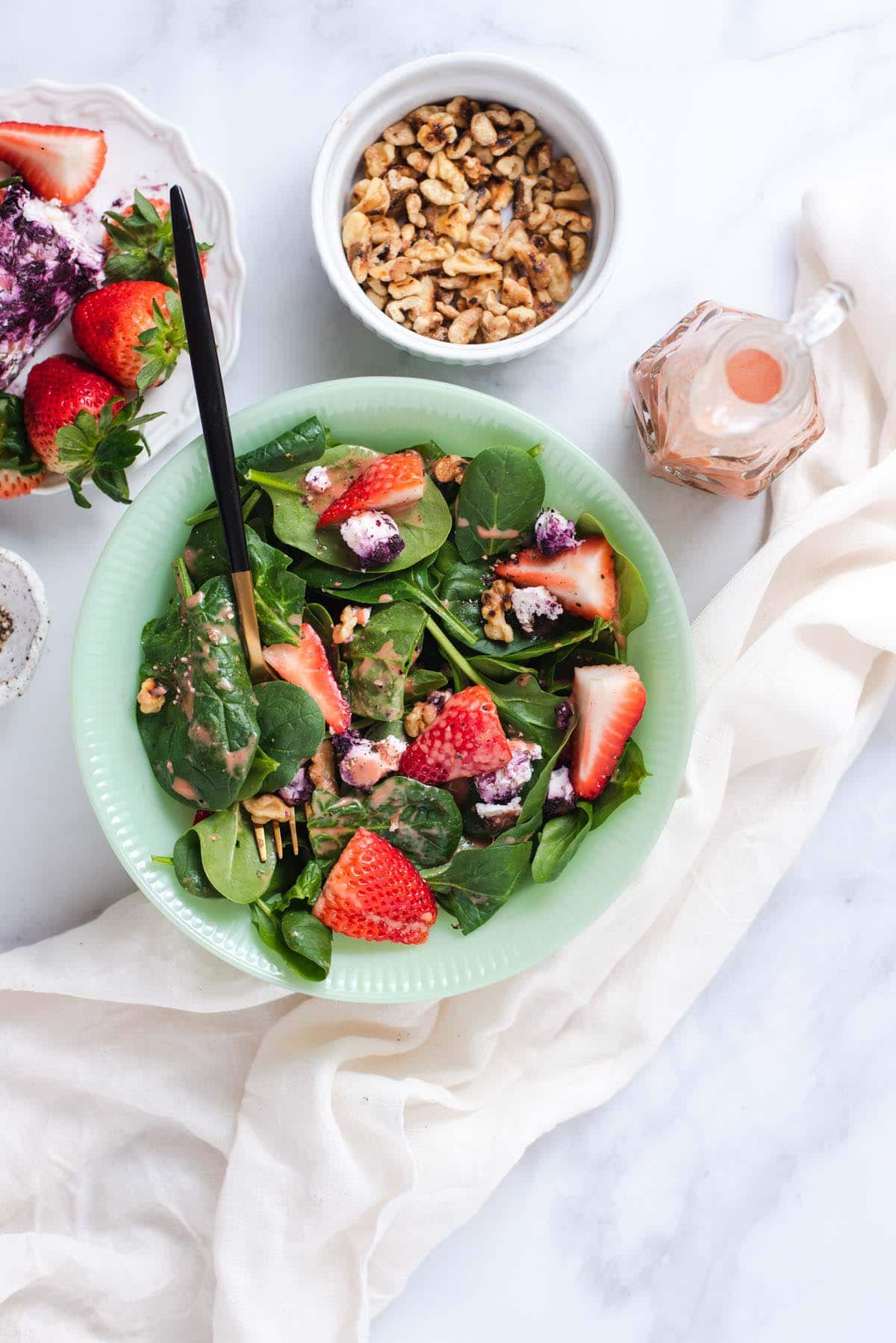 Overhead view of spinach and strawberry salad in a jade bowl on a marble background.