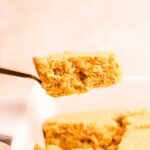 Gold fork lifting a slice of cornbread out of a white dish
