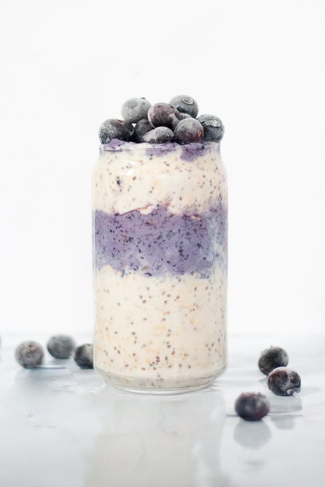 Side view of glass filled with white and purple oatmeal topped with blueberries