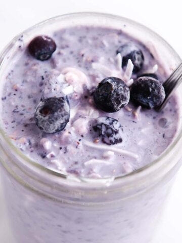 Purple coconut milk overnight oats in a glass jar topped with blueberries.