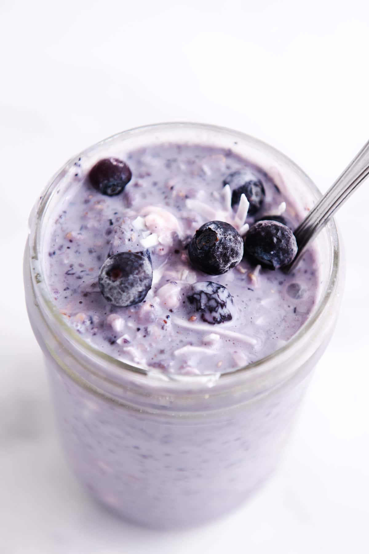 Purple blueberry overnight oats in a glass jar topped with blueberries.