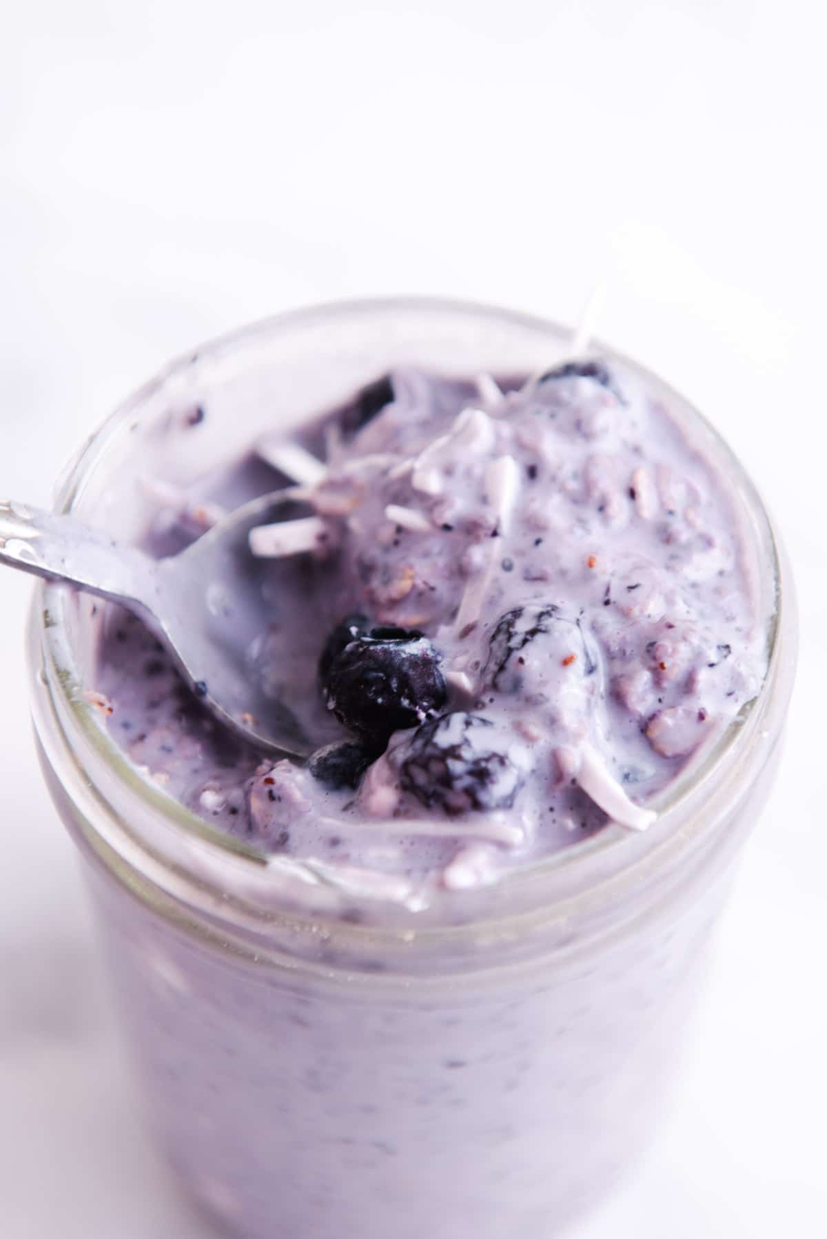 Spoon lifting blueberry overnight oats out of a glass jar