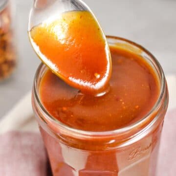 Silver spoon dripping BBQ sauce into jar of sauce