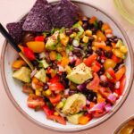 Overhead view of white bowl filled with black bean and corn salad with purple corn chips.