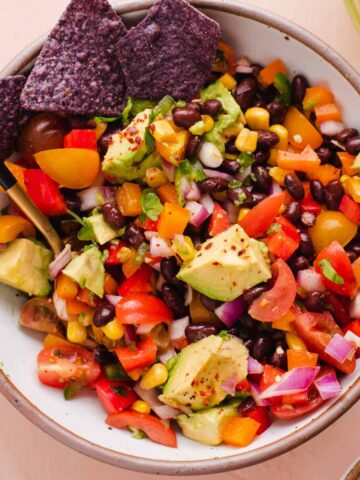Overhead view of white bowl filled with black bean and corn salad with purple corn chips.