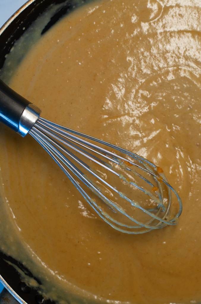 Close up of pasta sauce being whisked with a metal whisk in a large black sauce pan.
