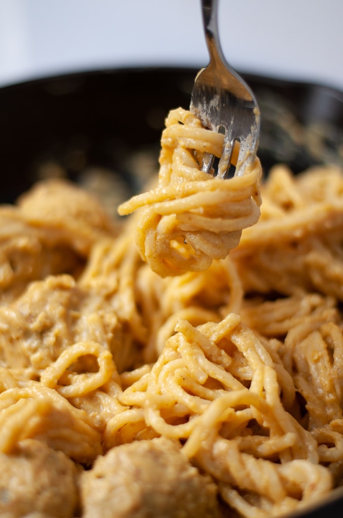 Silver fork twirling spaghetti noodles coated in pumpkin pasta sauce.