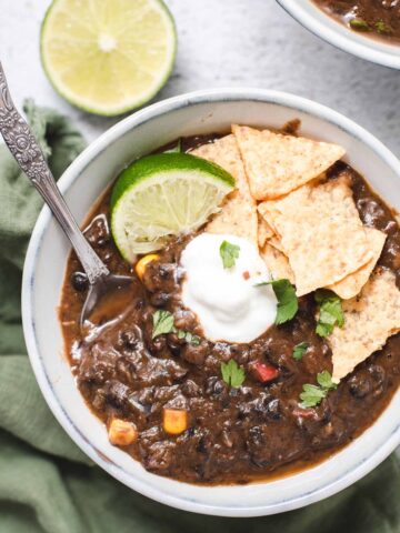 Close up of black bean soup in a gray bowl topped with cilantro, sour cream and a lime wedge