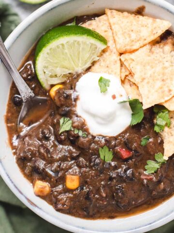 Close up of vegan black bean soup in a gray bowl topped with cilantro, sour cream and a lime wedge.