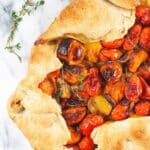 Galette with cherry tomatoes and fresh thyme on a marble table.