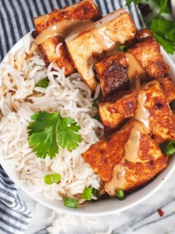 Tofu and rice in a white bowl with a drizzle of peanut sauce.