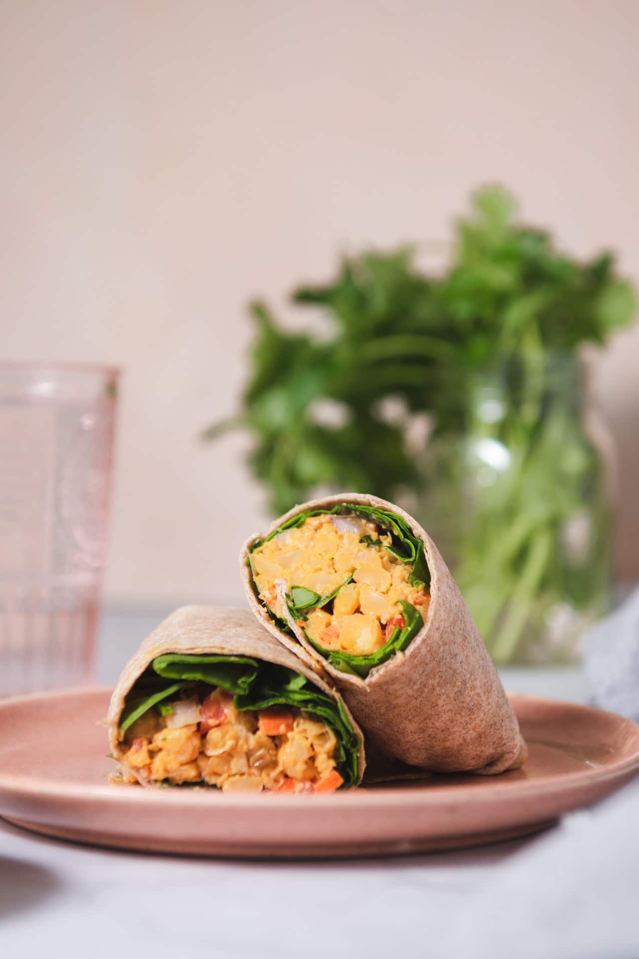 Two halves of a wrap on a pink plate with jar of cilantro in the background