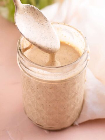 Tahini dressing dripping off of spoon into a glass jar of dressing.