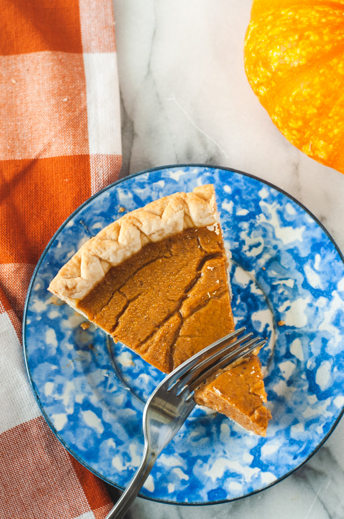 Pumpkin pie being sliced with a fork on a blue plate