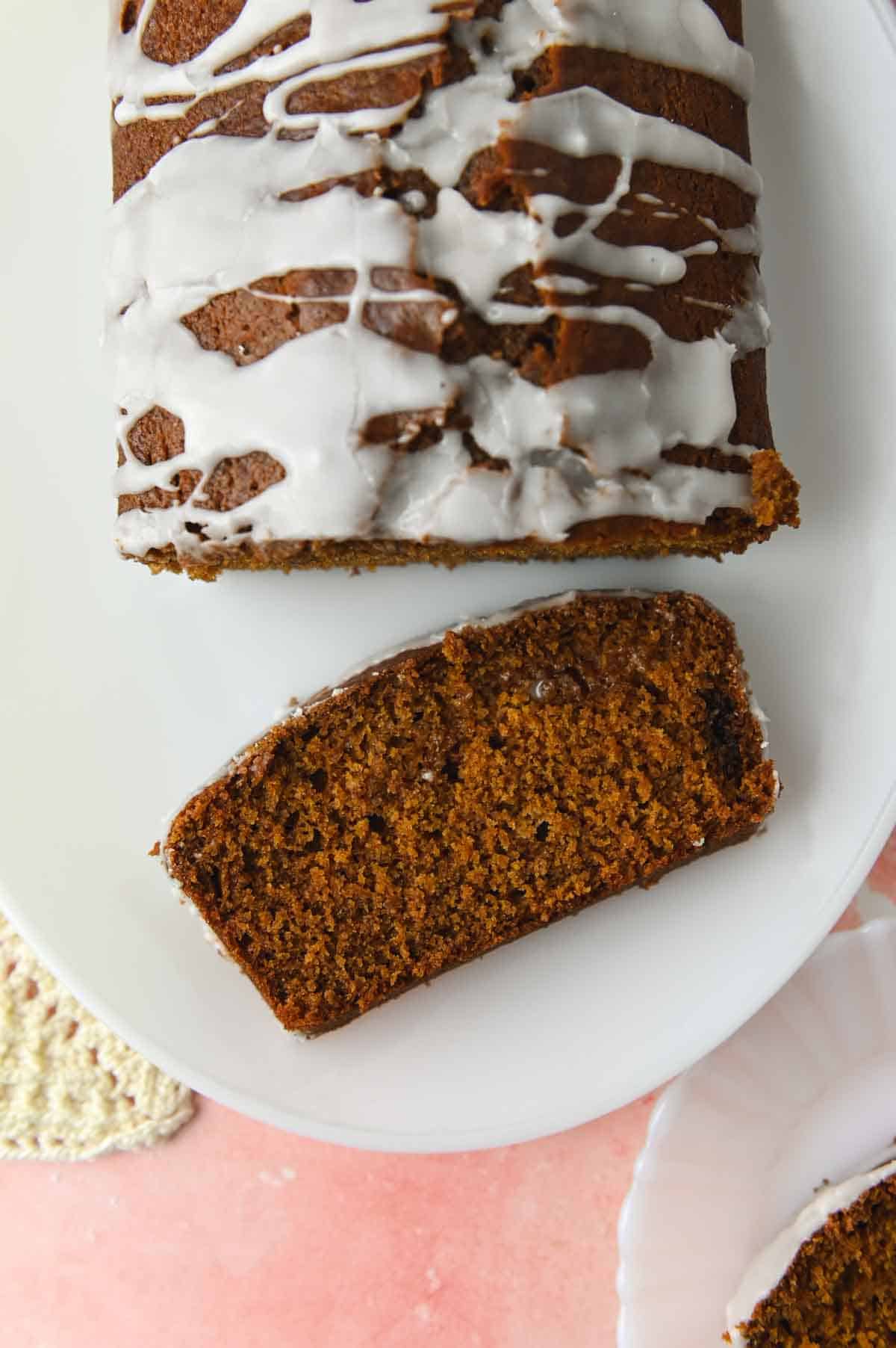 Slice of gingerbread loaf next to gingerbread on a white oval plate.