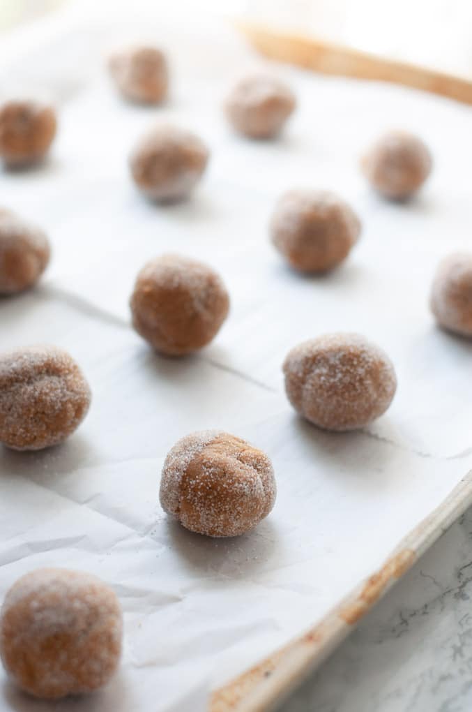 Cooke dough balls lined up on parchment paper lined baking sheet