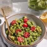 Side view of gray bowl filled with green pasta and cherry tomatoes