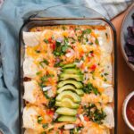 Overhead view of enchiladas in glass casserole dish topped with avocado and cilantro