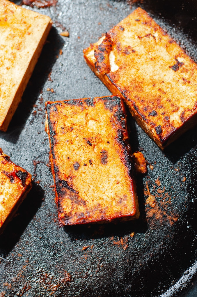 Crispy blackened tofu being pan fried in a cast iron pan.