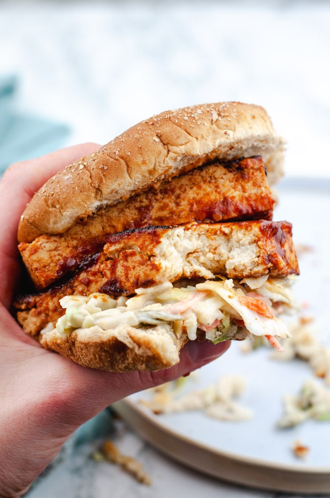 BBQ Tofu Sandwich being held in a hand. A bite is taken out of the sandwich.
