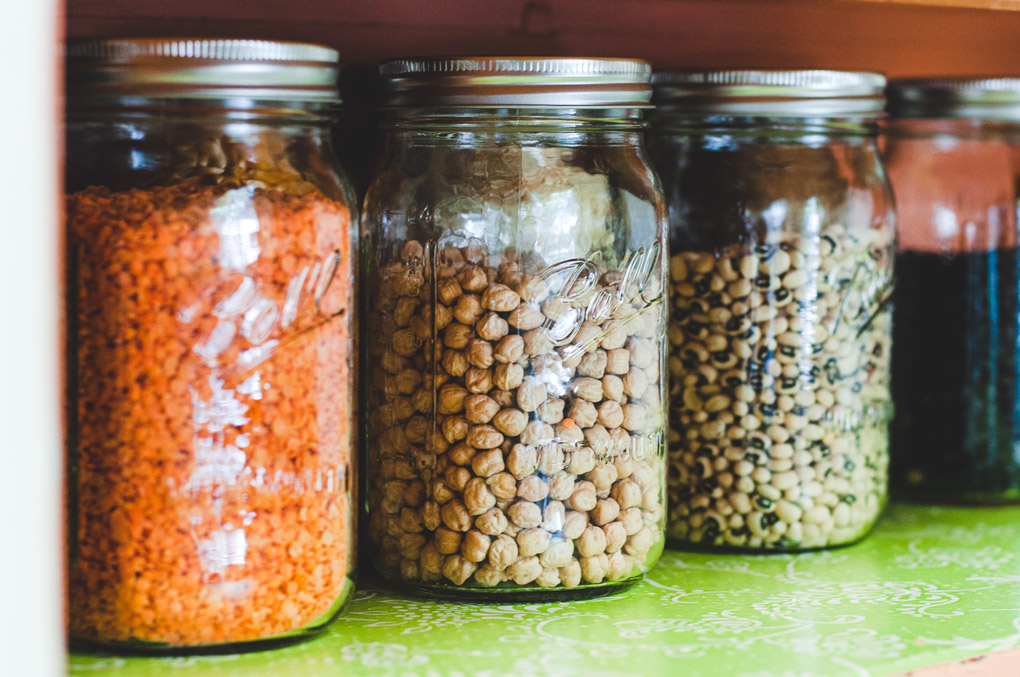 Ball jar filled with dry chickpeas next to two other jars sitting on a green shelf.