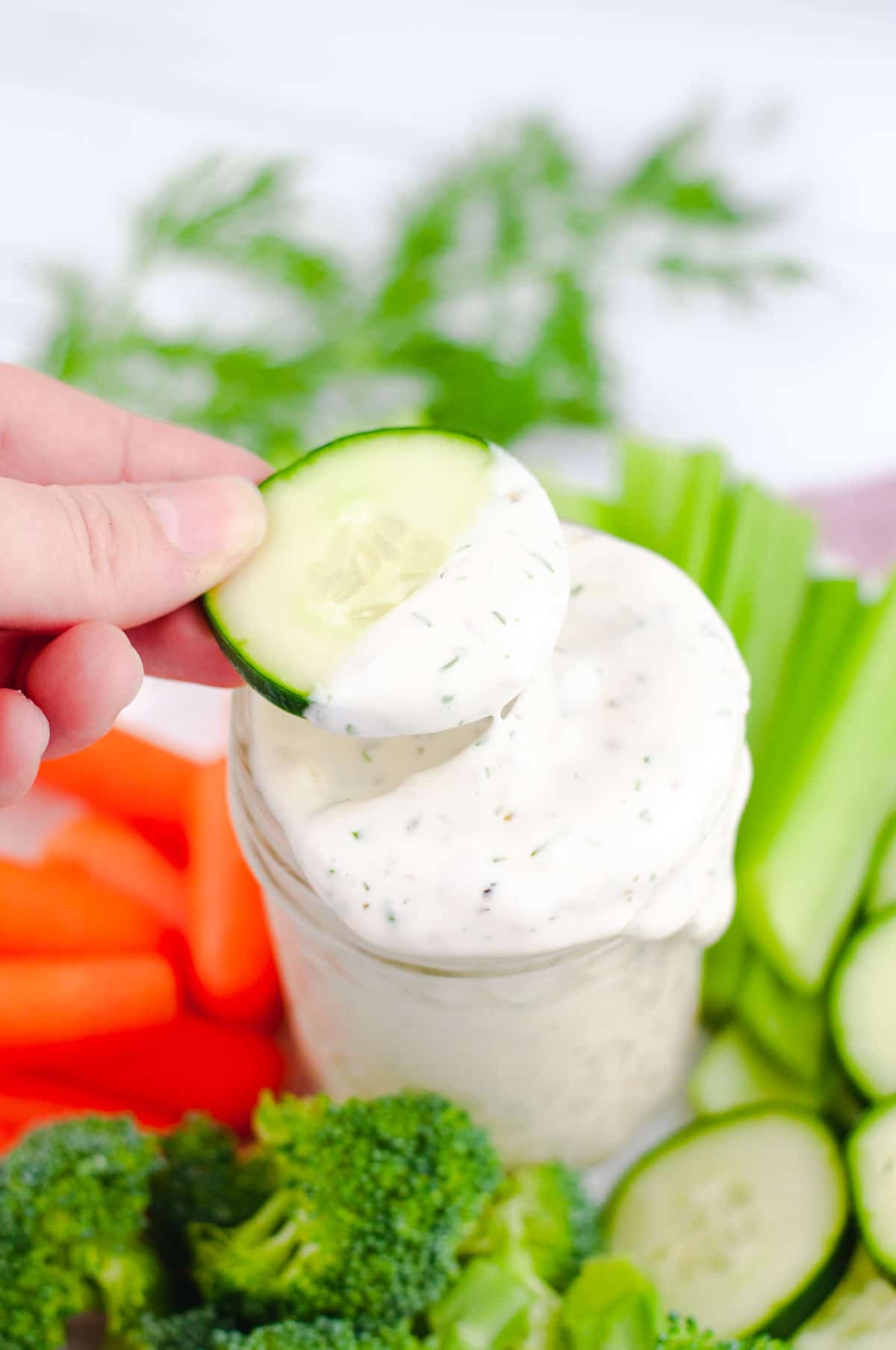 Slice of cucumber being lifted out of jar of ranch.