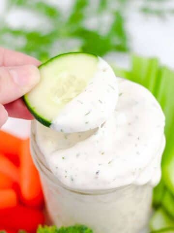 Slice of cucumber being lifted out of jar of ranch.
