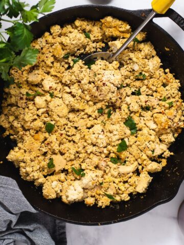 Overhead view of tofu scramble in cast iron pan next to pink plate and fresh parsley.