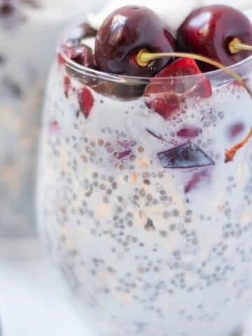 Cherry overnight oats in a glass topped with fresh cherries.