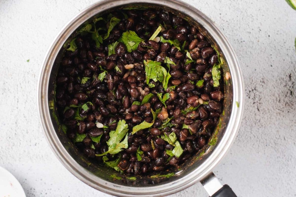 Overhead view of sauce pot filled with black beans and chopped cilantro.