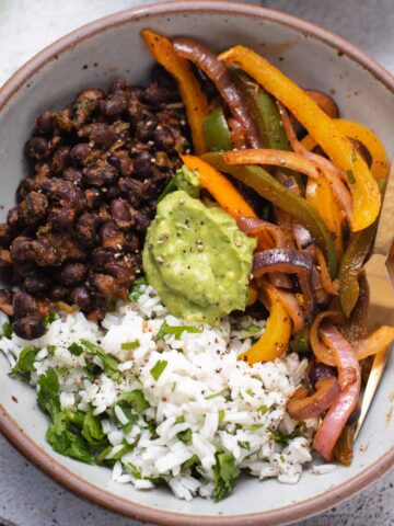 Overhead view of gray bowl filled with rice, fajita veggies, avocado cream and black beans.