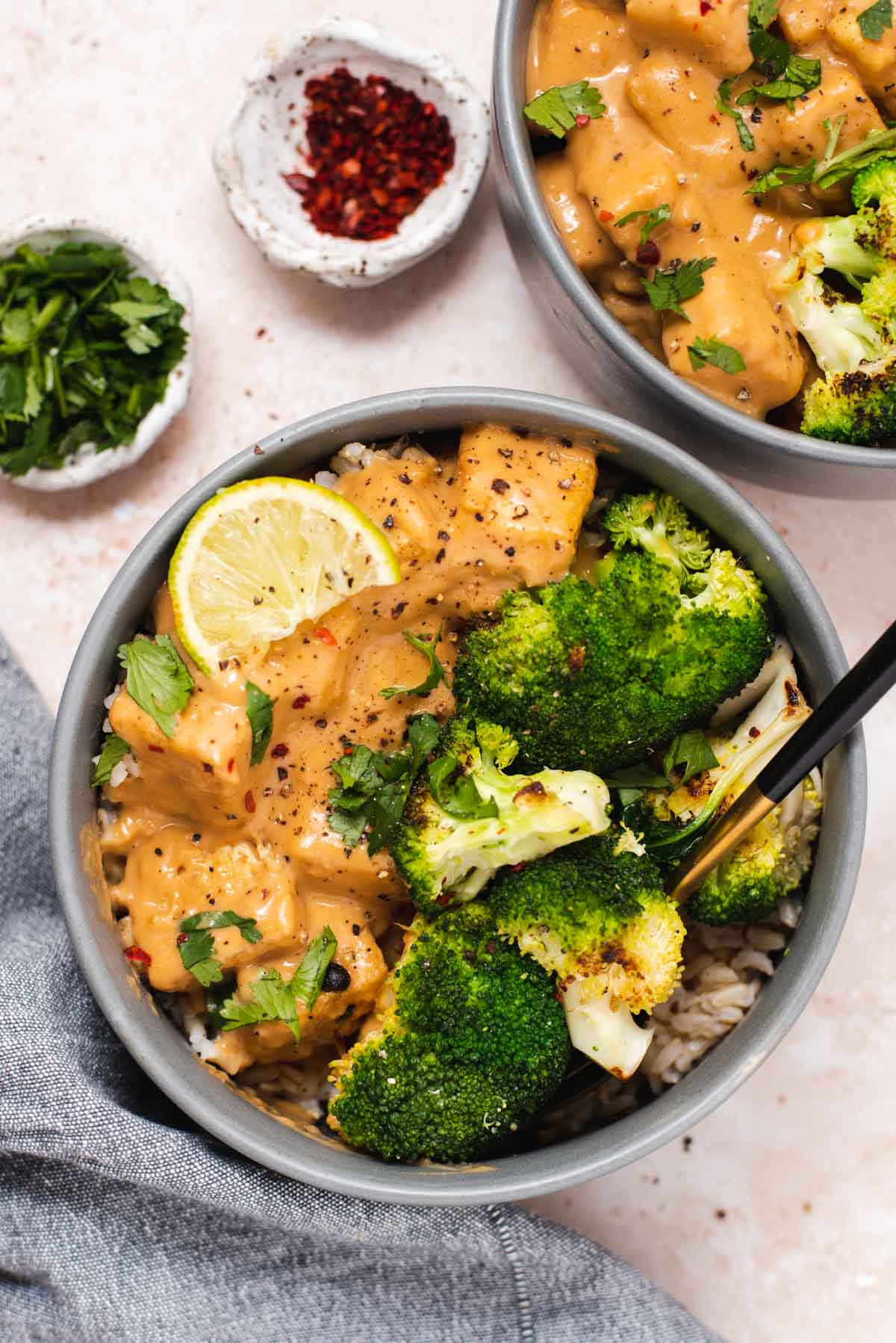 Overhead view of gray bowl filled with peanut tofu, broccoli and a lime wedge