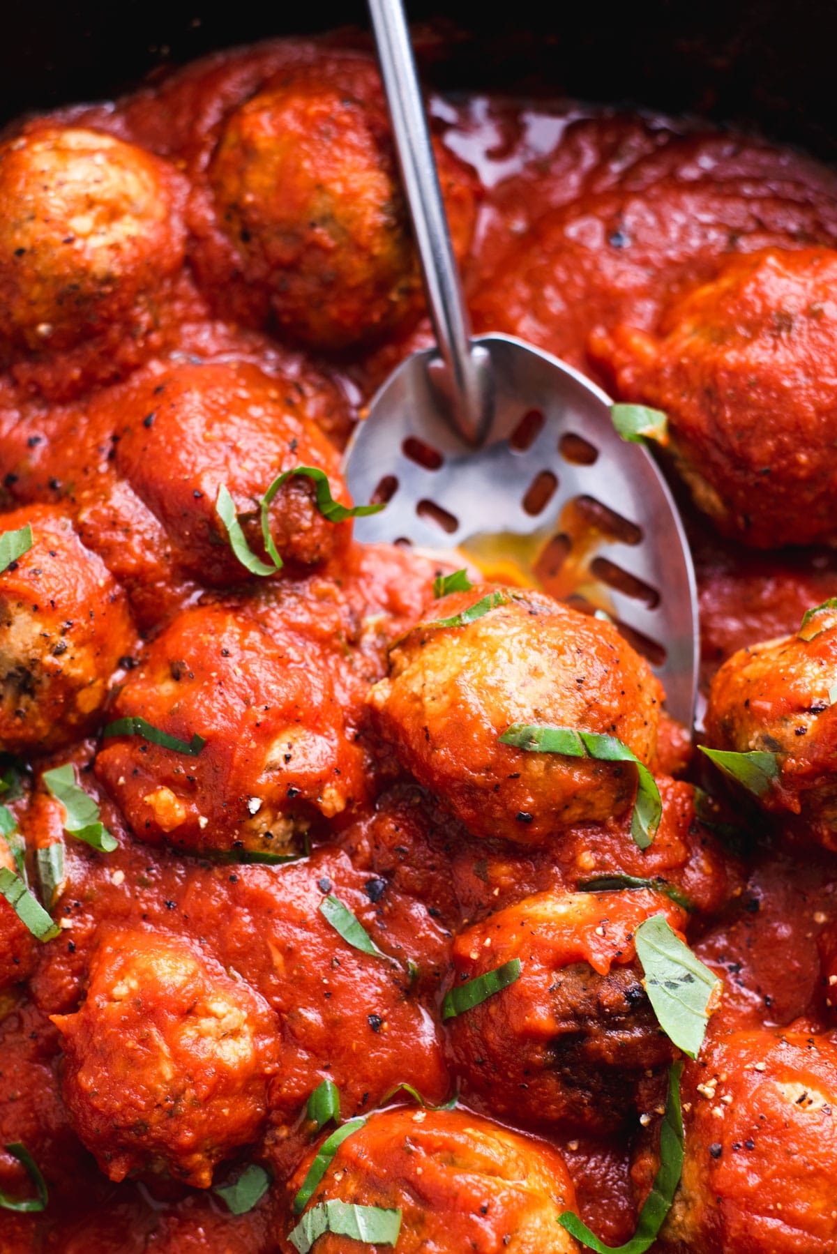 Close up of vegan meatballs in tomato sauce being lifted with a slotted spoon.