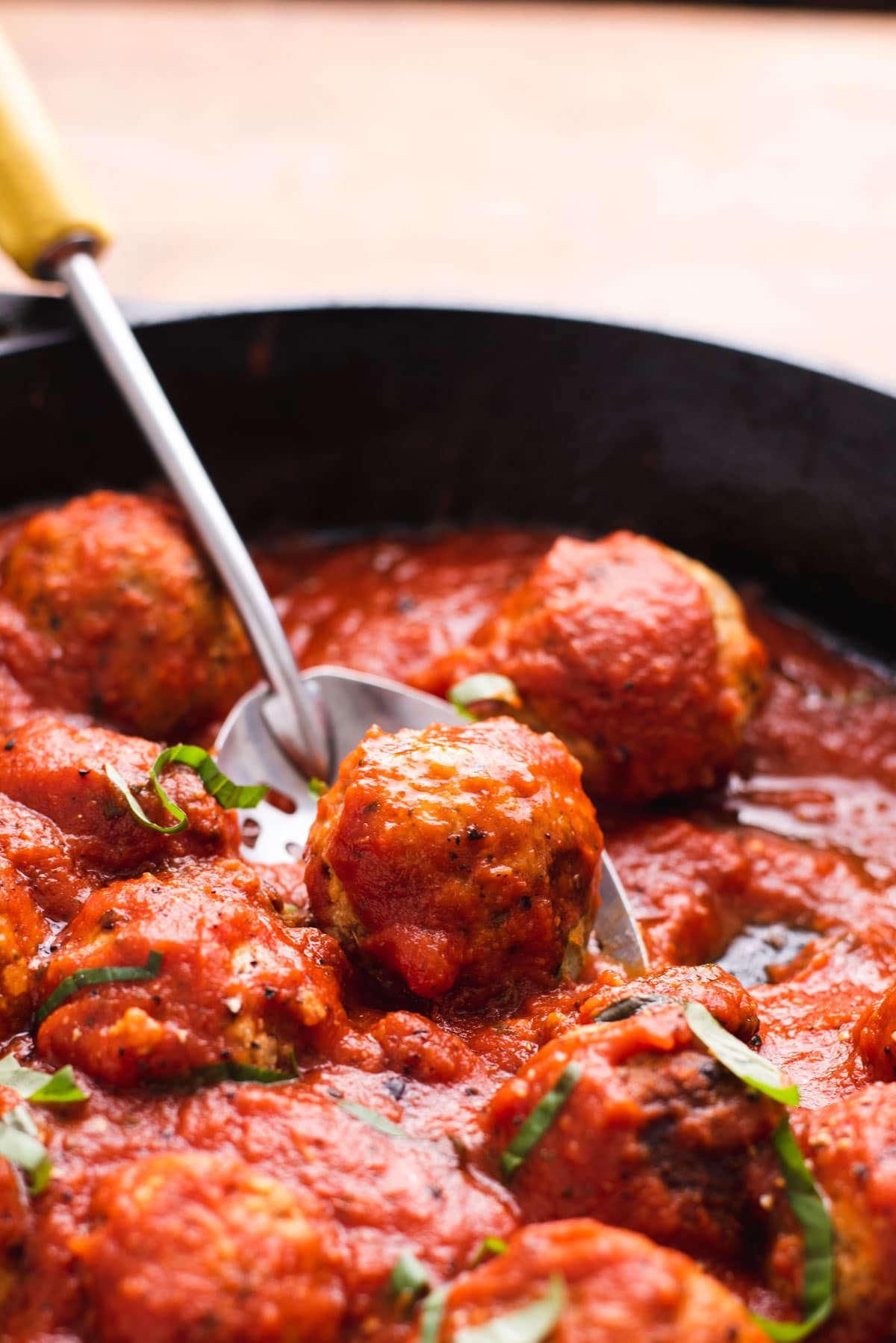 Meatball being lifting out of tomato sauce with metal serving spoon.