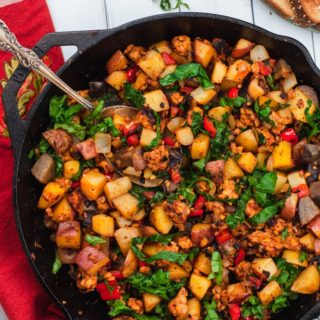 Potatoes, tempeh, and kale in a large cast iron skillet with a red clothe behind it.