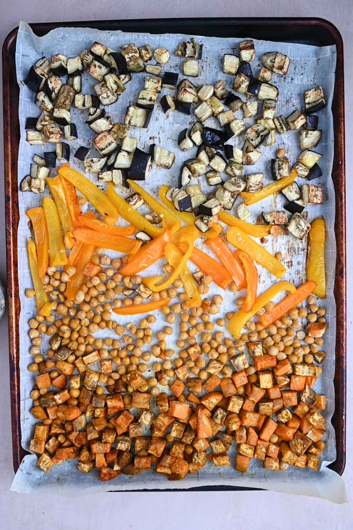 Bell pepper, eggplant, chickpeas, and sweet potato on a sheet pan after roasting.