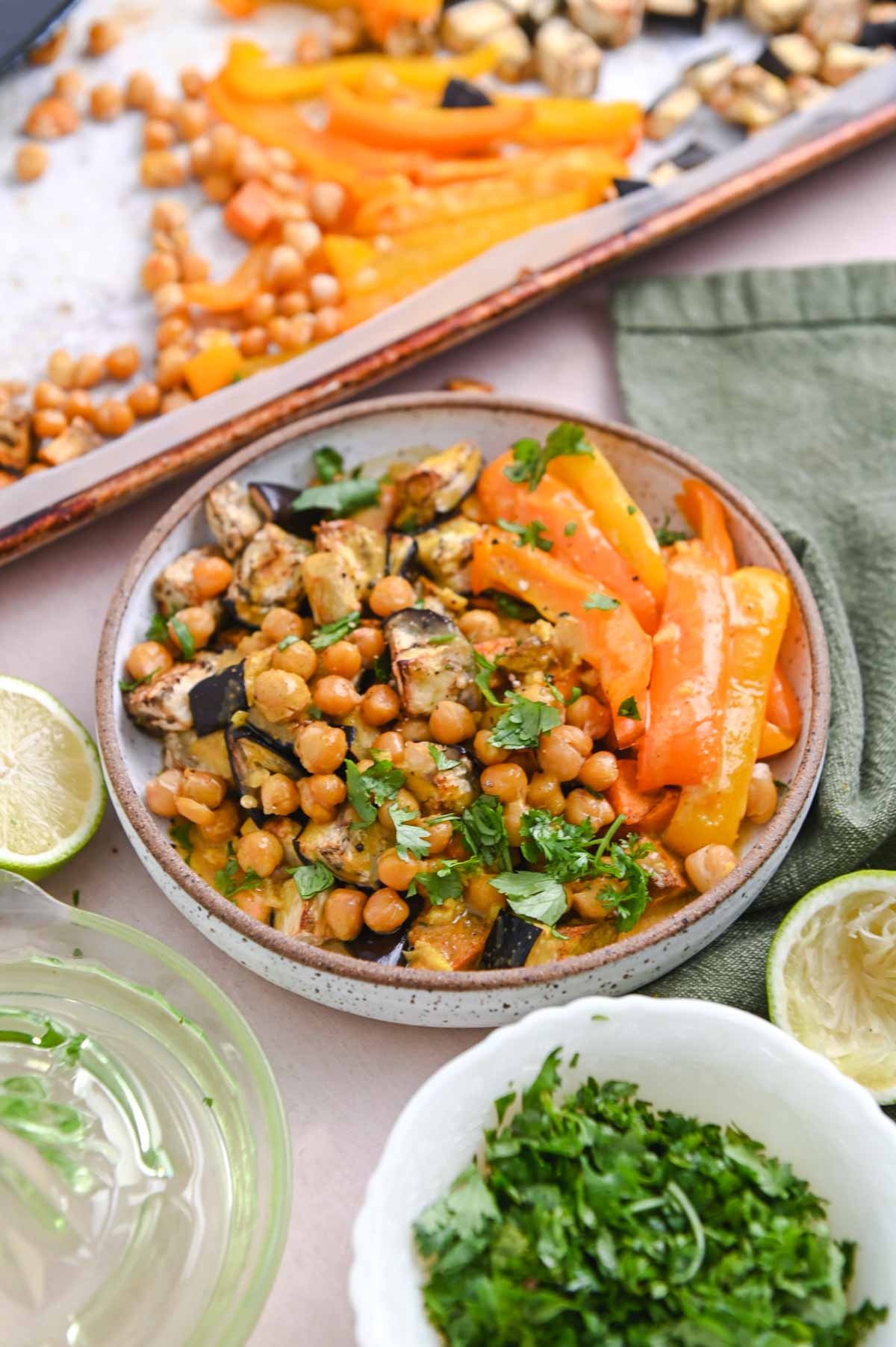Bowl of chickpeas and roasted vegetables in front of a sheet pan.