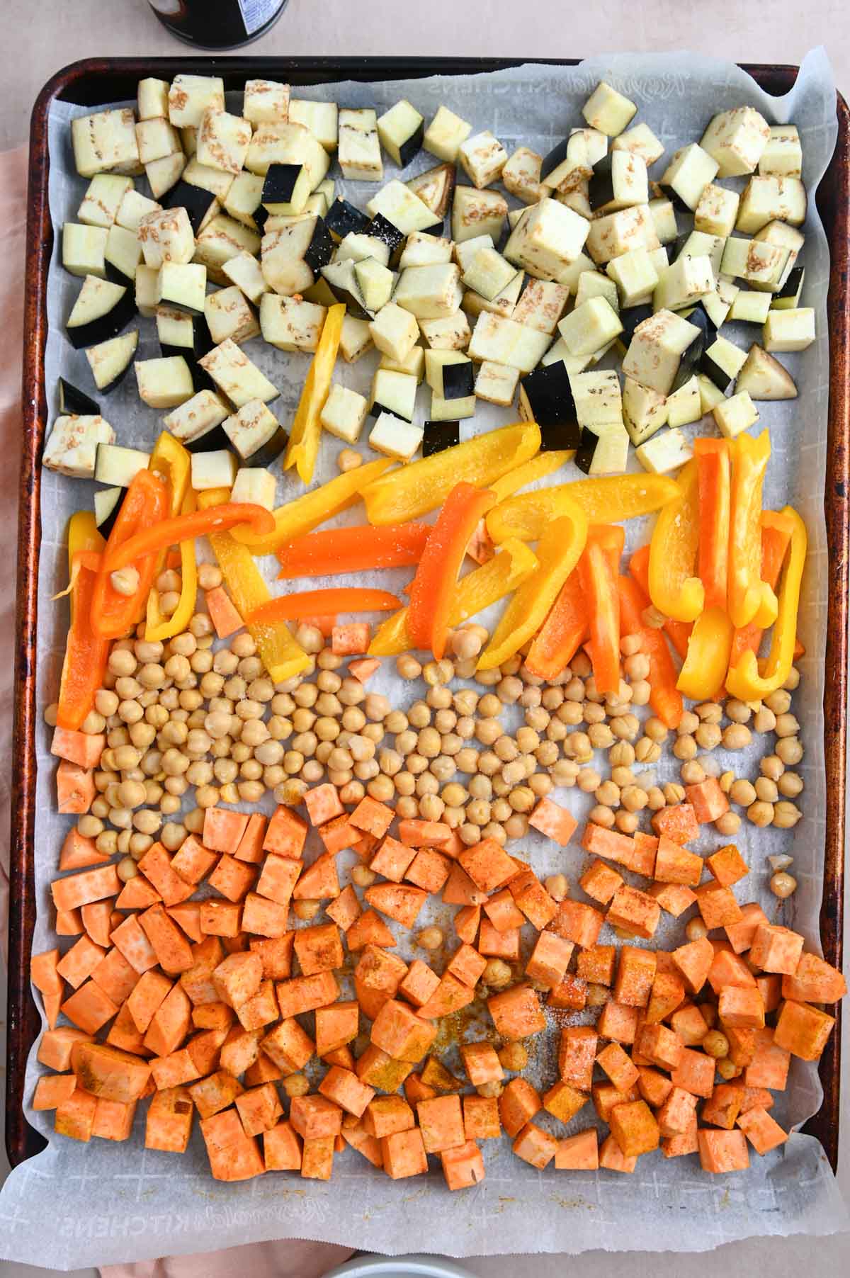 Bell pepper, eggplant, chickpeas, and sweet potato on a sheet pan before roasting.