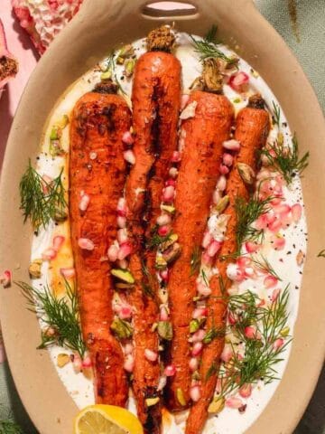 Four whole carrots on a bed of white whipped feta in a brown oval serving dish.