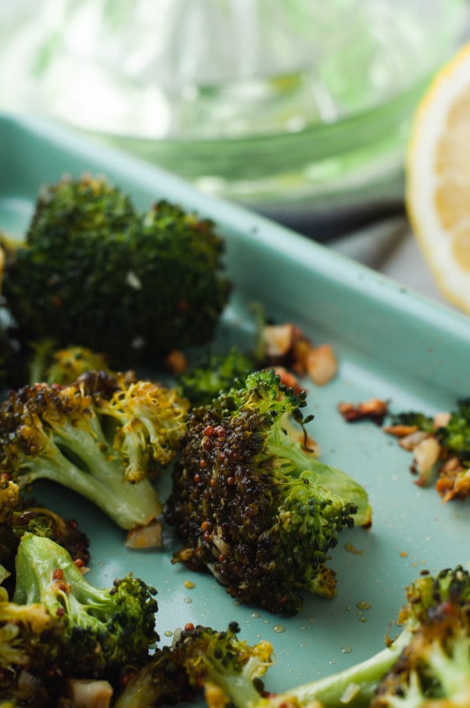 A few pieces of roasted broccoli lying on a sheet pan surrounded by minced roasted garlic.