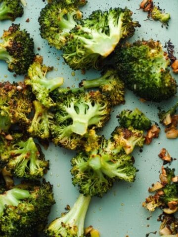 Close up of detail of roasted garlic broccoli on a blue sheet pan.