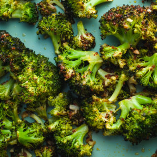 Close up of detail of roasted garlic broccoli on a blue sheet pan.