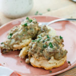 Two open face vegan biscuits topped with gravy and fresh sage on a pink ceramic plate.