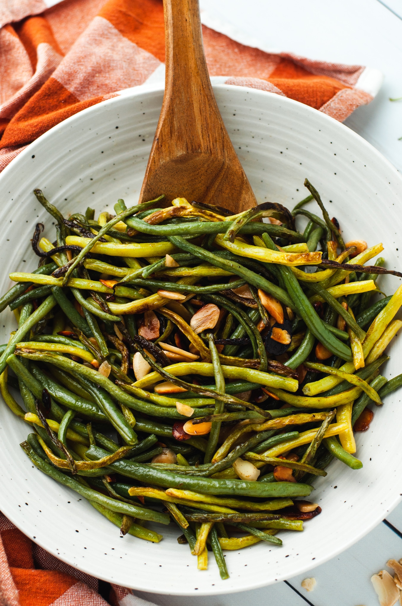 One recipe of green beans almondine in a white ceramic bowl with a wooden serving spoon.