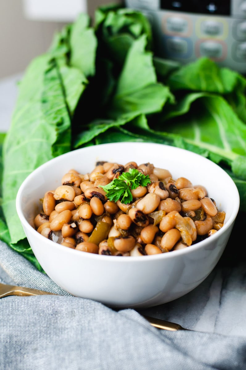 Small white bowl filled with instant pot black eyed peas with collard greens in the background