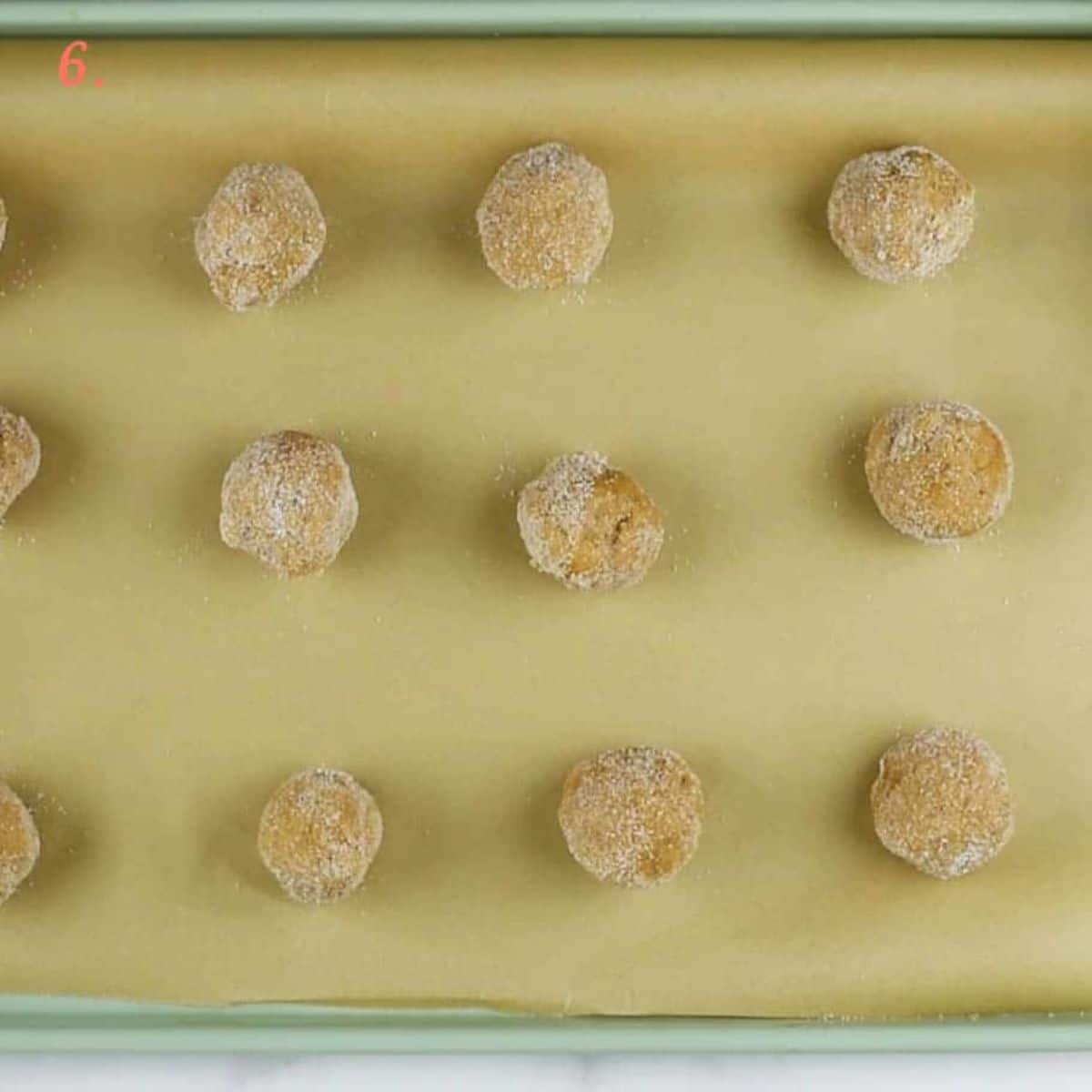 Twelve cookie balls on a parchment-paper lined baking sheet.