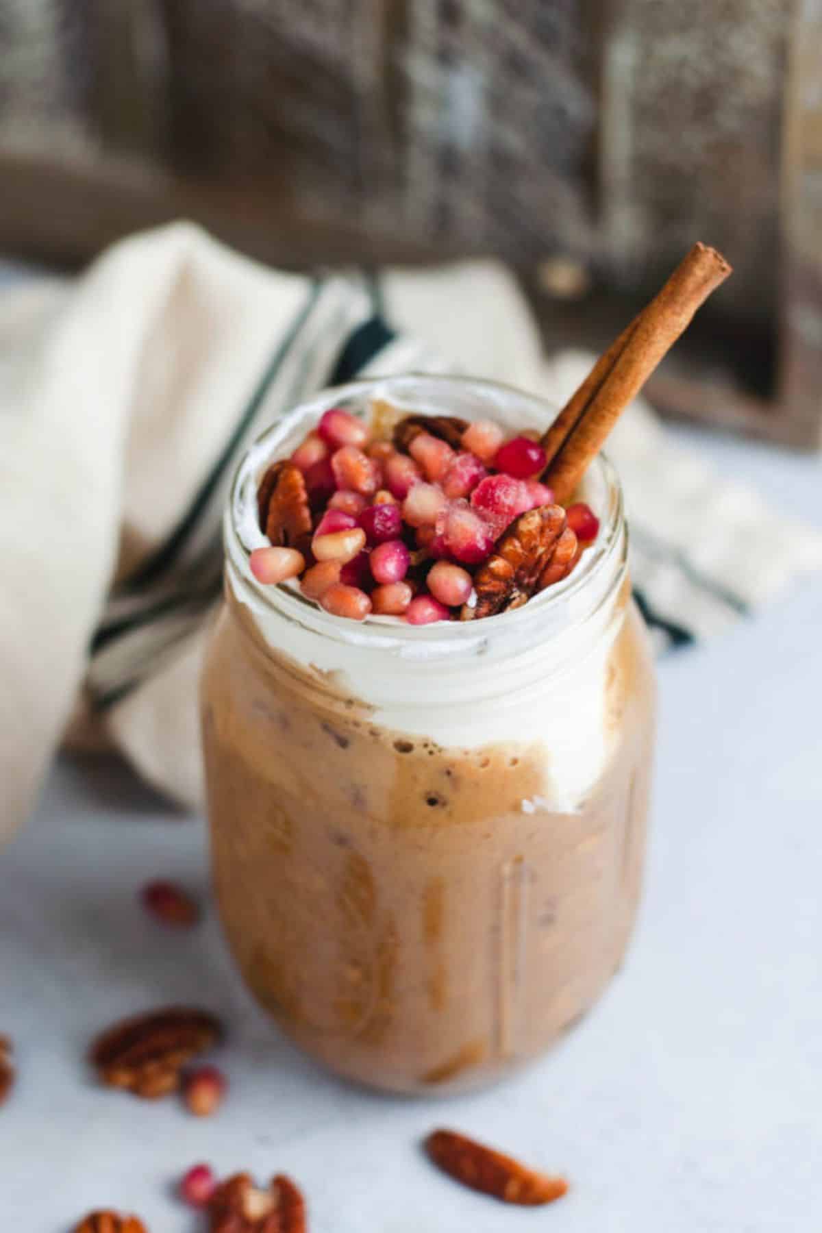 Glass jar filled with gingerbread oats that are topped with pomegranate seeds and a cinnamon stick.